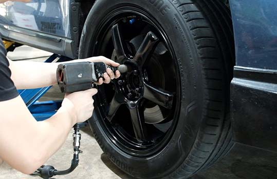 Picture of a KYC worker screwing a tyre back onto the car.