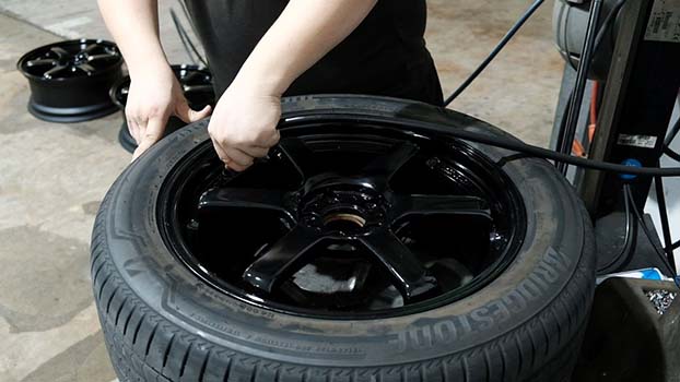 Picture of a KYC worker removing a tyre rim in the garage.