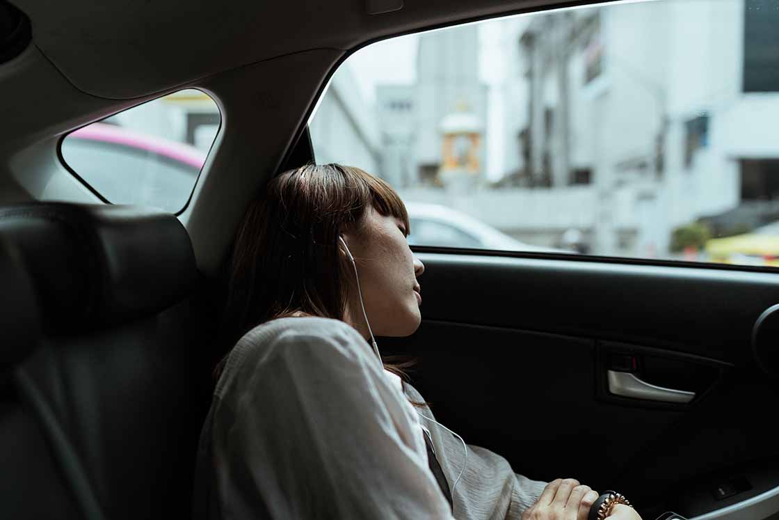 Picture of a girl in tranquil, with headphones on, in a moving car.