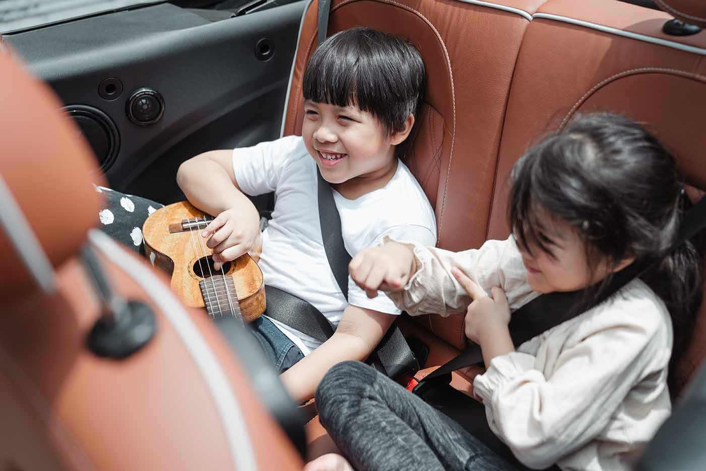 Picture of a child smiling and playing a guitar while sitting in a moving car.